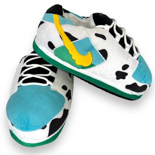 Low Moo Moo Sneaker Slippers – top view of cow-print plush sneaker-style slippers with teal soles and yellow swoosh accents.
